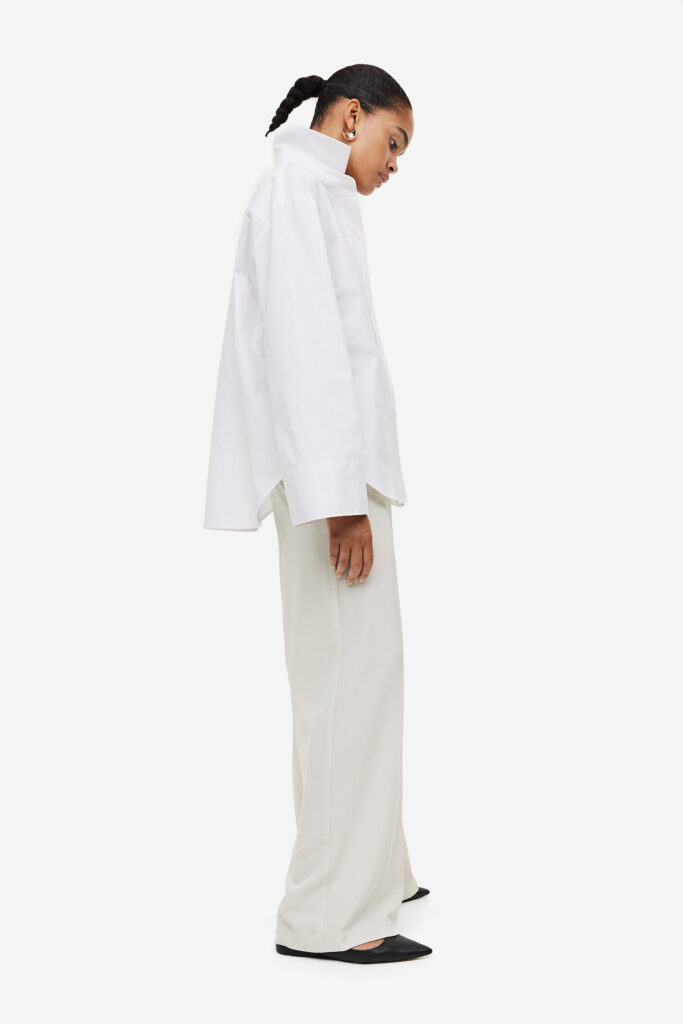 A woman wearing a crisp white button-down shirt, tailored beige trousers, and minimalist gold jewelry, embodying the clean girl aesthetic