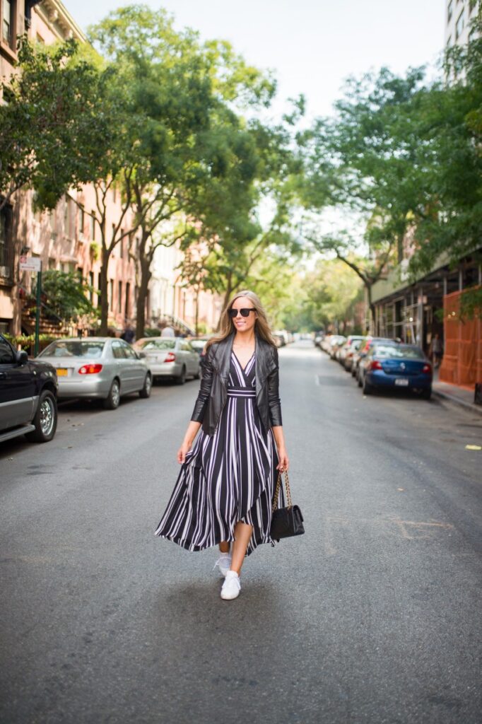 A woman confidently walking in a sleek black and white striped dress, holding a white clutch, showcasing a classic color combination