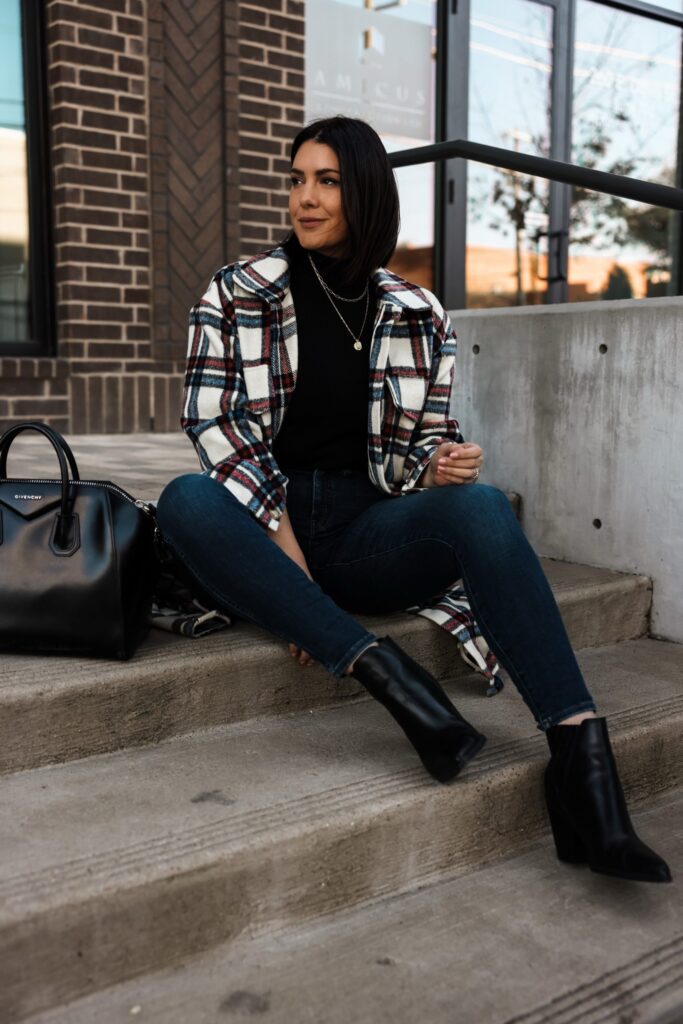 Woman wearing an oversized plaid shacket over a black turtleneck, with dark wash jeans and combat boots.