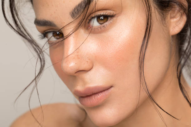 Close-up of a woman's face with dewy skin, natural brows, and a subtle pink blush, showcasing clean girl makeup